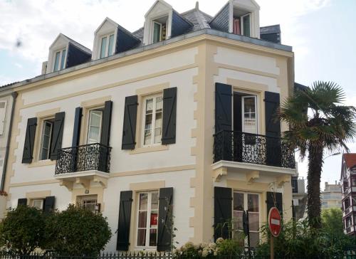 比亚里茨Maison Garnier Hôtel de Charme Biarritz的白色的房子,有黑色百叶窗和棕榈树
