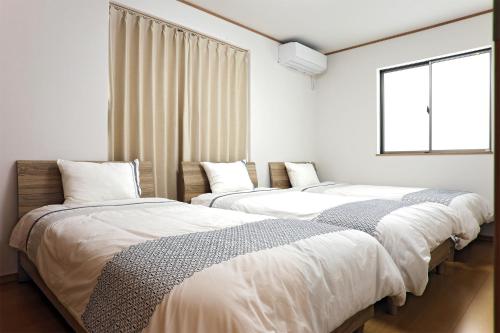 Agarii名護ビーチハウス的白色客房的两张床,设有窗户