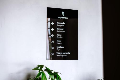 波德戈里察Hotel Septembar的白色墙上的黑色标志,带有植物