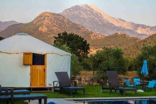卡亚克Yol Glamping的一个带椅子的帐篷和一个背景为山脉的游泳池