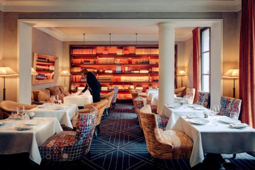 巴黎Le Pavillon de la Reine & Spa的一间设有桌椅的餐厅和一个站在房间里的人