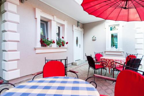 帕利克Vila Eden Palić的庭院设有红色椅子和一张带红色遮阳伞的桌子。