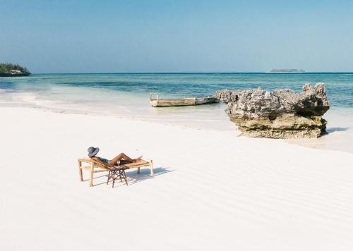 马特姆维Sunshine Bay Hotel Zanzibar的白色沙滩上的一张桌子和一把椅子