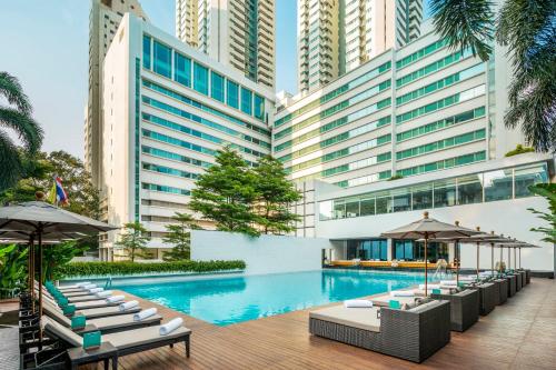 曼谷COMO曼谷大都会酒店的一张酒店游泳池的图片,里面摆放着椅子和遮阳伞