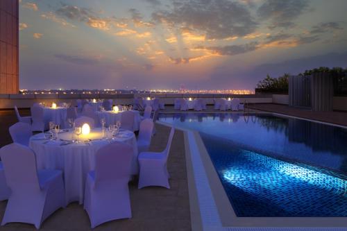 迪拜Millennium Central Downtown的一间设有白色桌椅的餐厅,位于游泳池旁
