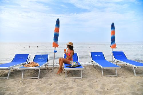 伊斯基亚Fortuna Beach - Seaside Hotel的坐在海滩上的女人,带椅子和遮阳伞