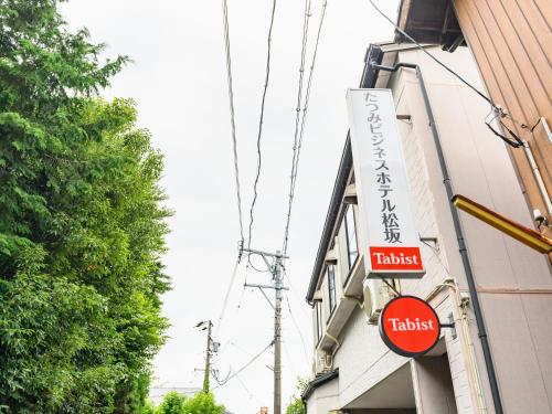 松阪市Tabist Tatsumi Business Hotel Matsusaka的大楼一侧酒店标志