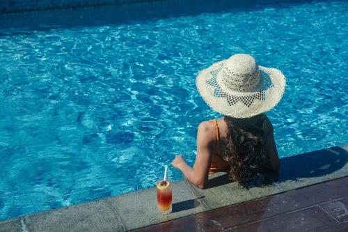 沙努尔Holiday Inn Bali Sanur, an IHG Hotel的坐在游泳池边喝一杯的戴帽子的女人