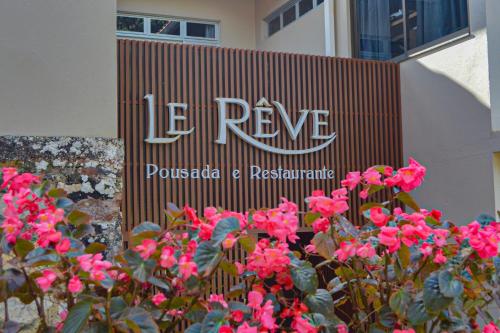 瓜拉米兰加Le Rêve Pousada e Restaurante的粉红色花卉建筑前的标志