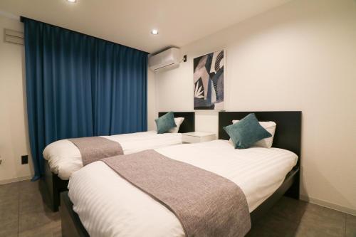 札幌TAKETO STAY Sumikawa House的两张位于酒店客房的床,配有蓝色窗帘