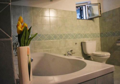 马斯卡利Peri Peri Guest House的浴室设有浴缸,花瓶上装有黄色花卉