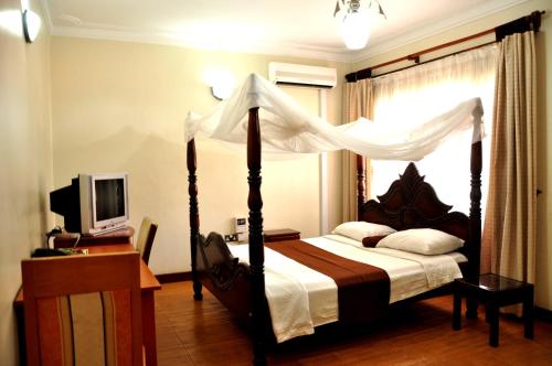 坎帕拉Olive Gardens Hotel Kampala的一间卧室配有一张天蓬床和一台电视机