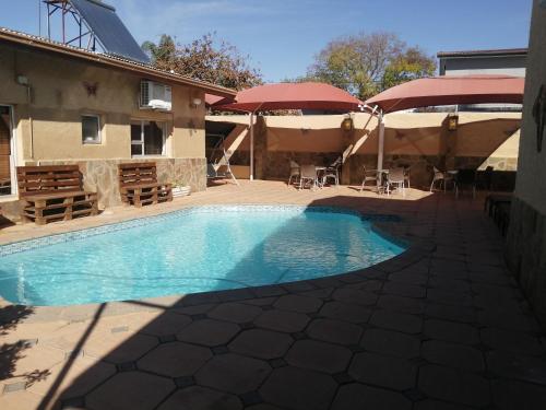 温特和克Esperanca Guesthouse的一座带桌子和遮阳伞的游泳池位于一座建筑旁边