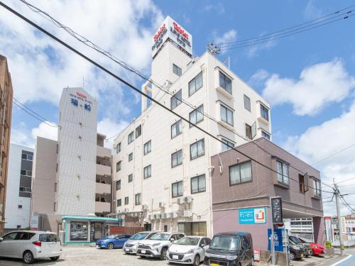 宫崎Tabist Rays Hotel Yakata的一座高大的白色建筑,汽车停在停车场