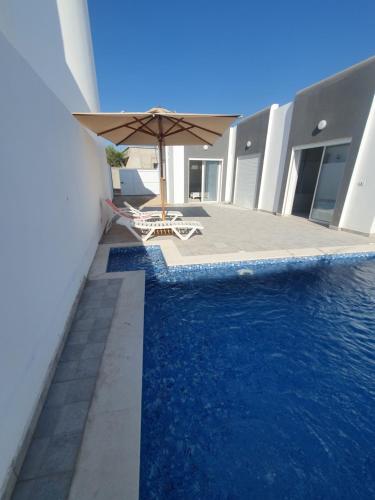 阿格希尔Villa de luxe avec piscine sans vis à vis Midoun的一座带遮阳伞和椅子的游泳池位于大楼旁