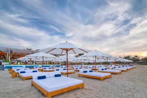阿布扎比Radisson Blu Hotel & Resort, Abu Dhabi Corniche的海滩上的一组沙滩椅和遮阳伞