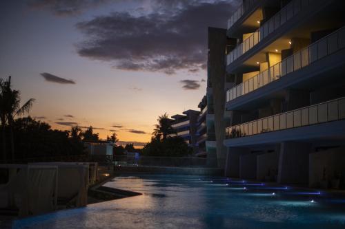 普拉亚卡门Palmaïa The House of AïA All Inclusive Wellness Resort的日落时分在建筑物前的一个空游泳池