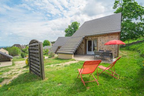 奥蒙奥布拉克Village de gîtes Les Chalets de l'Aubrac的一座房子,配有两把椅子和一把红色雨伞