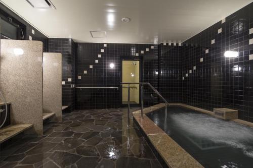 出云市Green Rich Hotel Izumo (Artificial hot spring Futamata Yunohana)的浴室设有黑色瓷砖和热水浴缸。