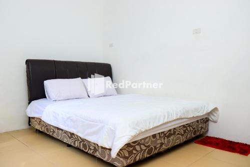 TanjungbingaSahabat Pantai Guest House Mitra RedDoorz的一张带白色床单和黑色床头板的床