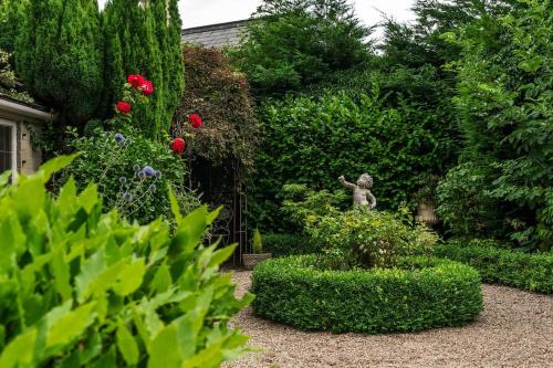 佩恩斯威克Lovedays Cottage, A Luxury 16th Century home in Painswick的一座花园,花园内有雕像、鲜花和灌木