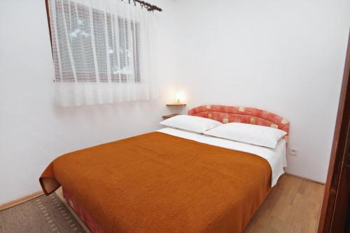 泰斯Apartments by the sea Nemira, Omis - 5884的一间卧室配有一张带橙色毯子和窗户的床。