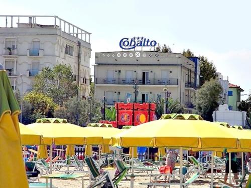 里米尼克巴尔托酒店的海滩上设有黄色的遮阳伞和椅子,还有一座建筑