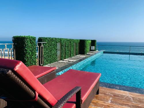 普里The Bay Suites的毗邻大海的游泳池,设有红色长椅