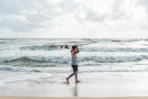 蔻立Kokotel Khao Lak Lighthouse - SHA Extra Plus的头上冲浪板在海滩上行走的男人