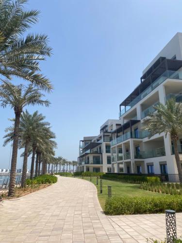 富查伊拉Two Bedroom Apartment Address Residence - Fujairah的海滩上的一座建筑,种植了棕榈树,设有人行道
