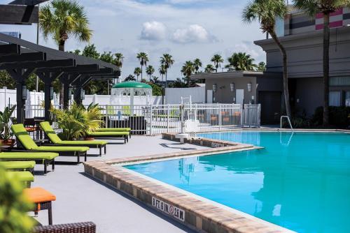 奥兰多Holiday Inn & Suites Across From Universal Orlando, an IHG Hotel的一座游泳池,里面设有绿色的躺椅和棕榈树