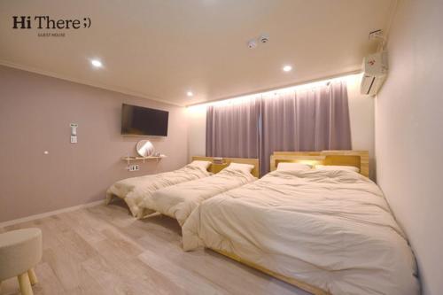 首尔Hithere guesthouse的卧室设有两张床,墙上配有电视。