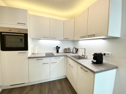 腓特烈港Auszeit Apartment STYLE am Uferpark - nur 100 m bis zum Bodensee, direkt am Bodenseeradweg, Sonnenbalkon, schnelles WLAN, kostenloser Tiefgaragenstellplatz, für bis zu 2 Personen的白色的厨房配有白色橱柜和水槽