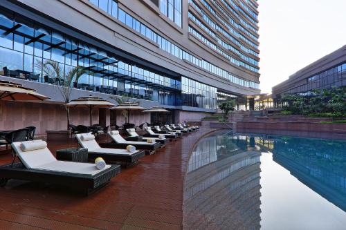 加尔各答加尔各答诺富特酒店及公寓的一座酒店,毗邻一座建筑,设有游泳池和躺椅