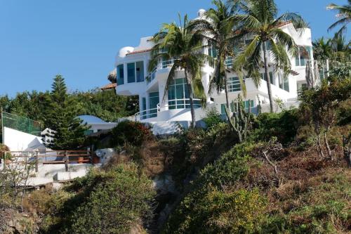 安赫尔港Hermosa Villa con alberca infinita Playa Zipolite的棕榈树山丘上的白色房子