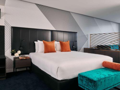 墨尔本Movenpick Hotel Melbourne On Spencer的卧室配有带橙色枕头的大型白色床
