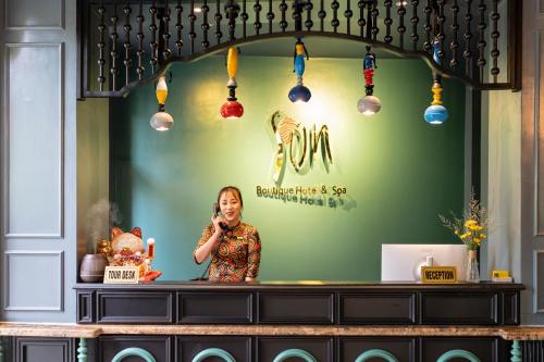 会安Son Hoi An Boutique Hotel & Spa的站在柜台后面的一位女士在手机上讲话