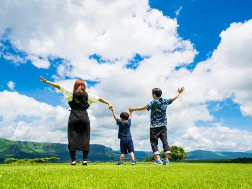 阿苏市格兰德里奥麻生度假酒店的一名妇女和两名男孩站在田野上,手臂伸出
