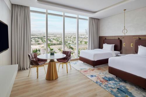 迪拜Movenpick Jumeirah Village Triangle的酒店客房,设有两张床和一张桌子,椅子