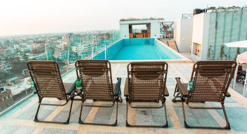 拉杰沙希Royal Raj Hotel的三把椅子坐在一座带游泳池的建筑的顶部