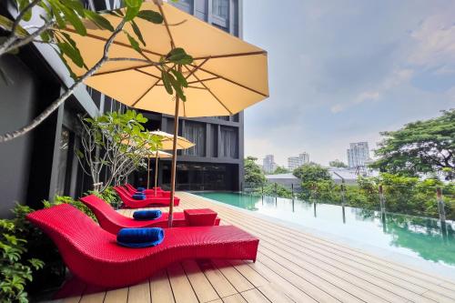 曼谷曼谷素坤逸奥克伍德华庭工作室酒店的一个带红色椅子和遮阳伞的甲板和游泳池