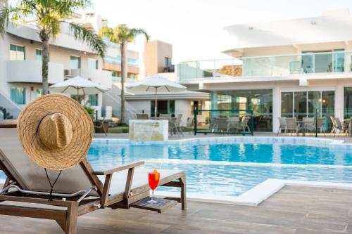 邦比尼亚斯Makkai Resort Bombinhas的坐在游泳池旁椅子上的草帽