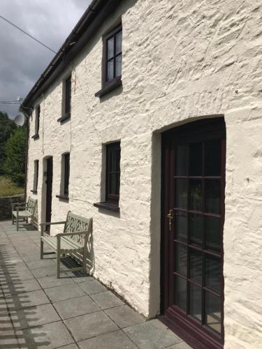 布雷肯Cobblers Cottage in Brecon Beacons的白色的建筑,有两把长椅和门