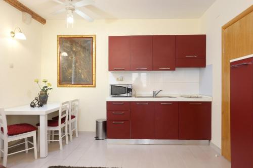 特罗吉尔Apartments by the sea Trogir - 19575的厨房配有红色橱柜和白色桌子