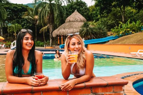 AmagáHotel Hacienda la Bonita的两个女人坐在游泳池旁边,喝着饮料