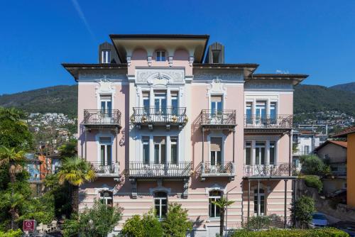 洛迦诺亚历山德拉酒店的一座粉红色的建筑,设有阳台,位于山丘上