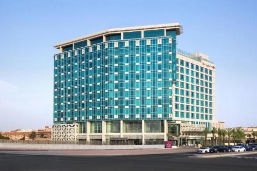 吉达Crowne Plaza - Jeddah Al Salam, an IHG Hotel的一座高大的玻璃建筑,前面有汽车停放