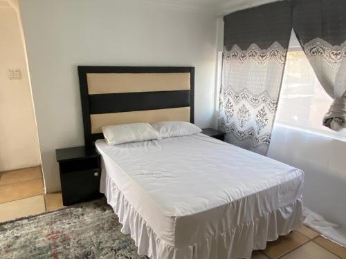 索韦托Soweto Towers Guest Accommodation的一间卧室配有一张带白色床单的床和一扇窗户。