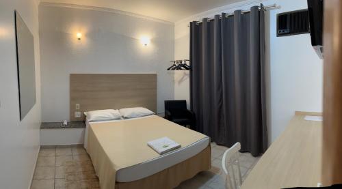 坎皮纳斯Hotel Taquaral的小房间设有床、书桌和窗帘
