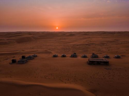 ShāhiqSands Dream Tourism Camp的日落时分在沙漠中停放的一群汽车